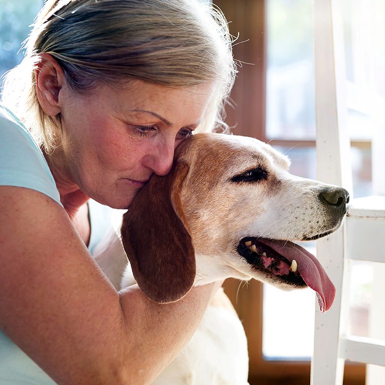 a woman holding a white dog with brown ears near a white chair