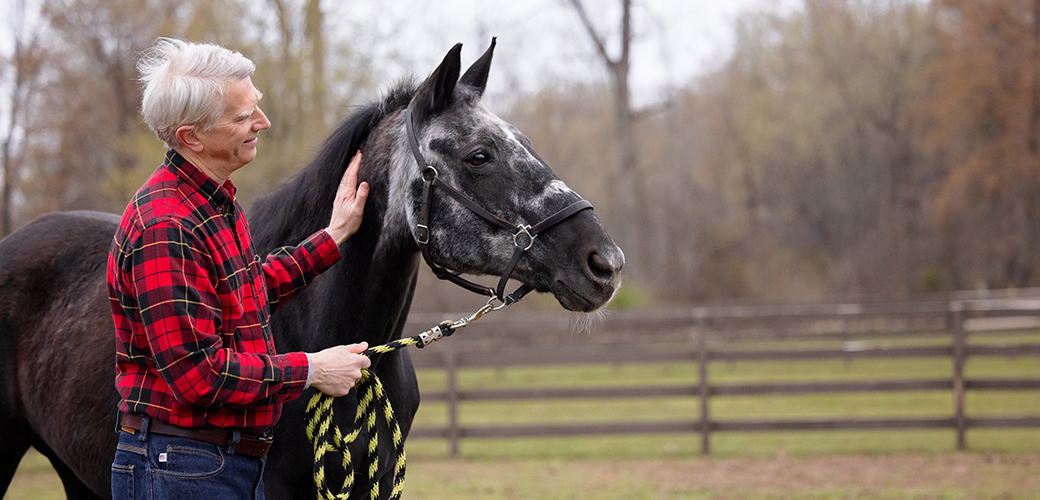 an older man wearing red plaid walking next to a horse