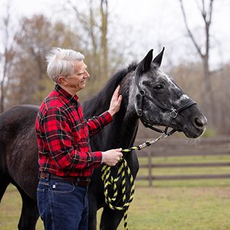 an older man wearing red plaid walking next to a horse